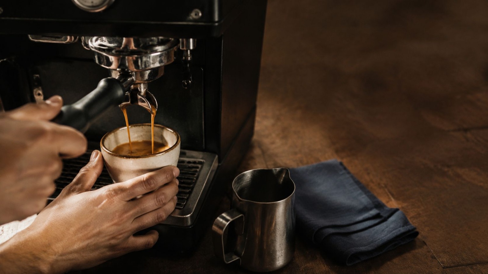 Close-up of an espresso shot being extracted into a ceramic cup at a Northpoint machine, with a milk jug and navy cloth on a dark wooden counter