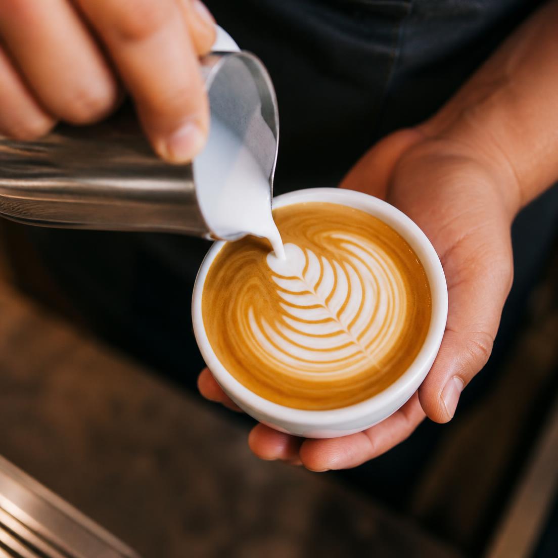 Barista pouring latte art into a takeaway cup